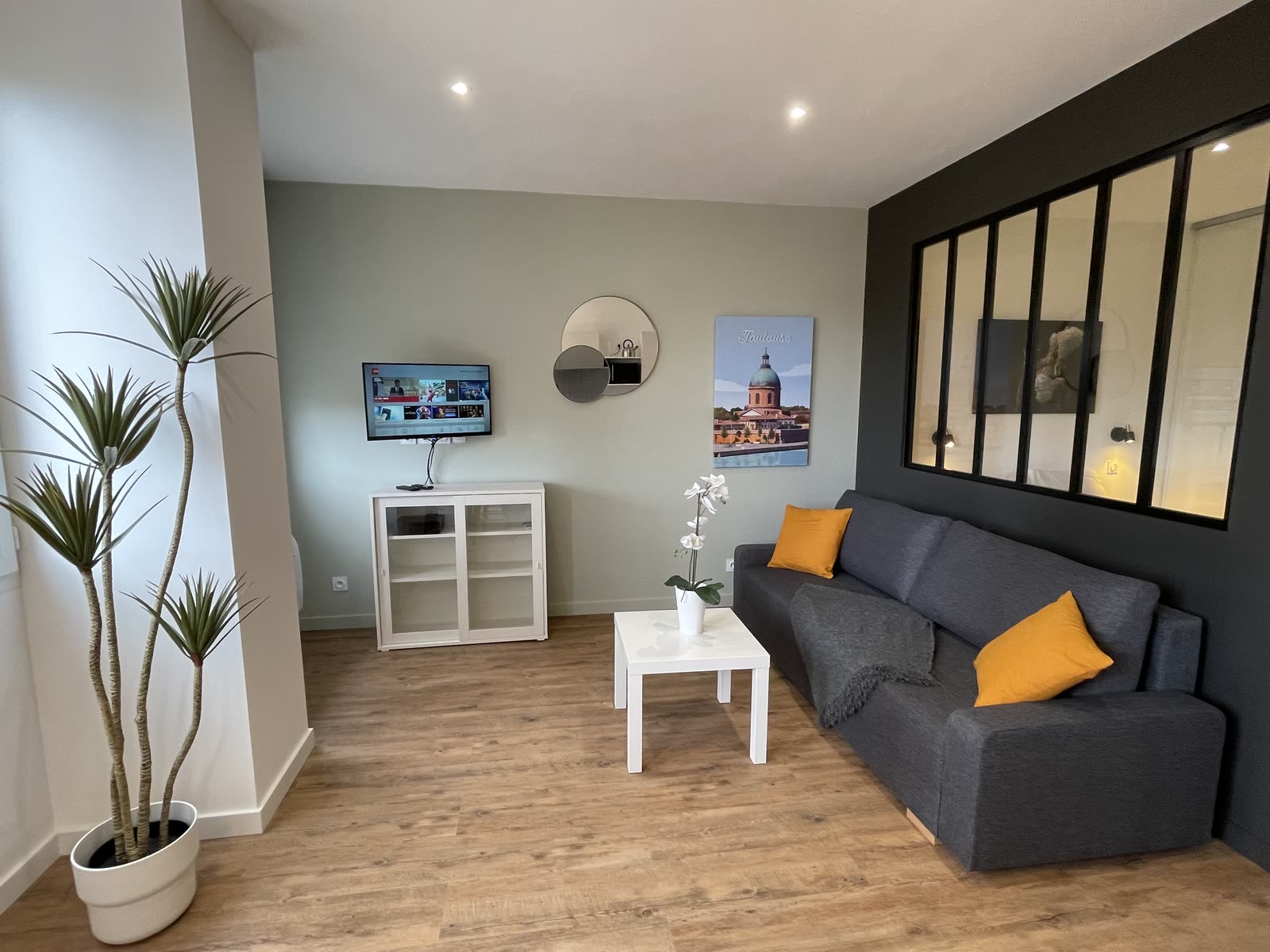 Séjour d'un appartement toulousain géré par Takeys : verrière d'atelier, parquet clair et affiche de Toulouse